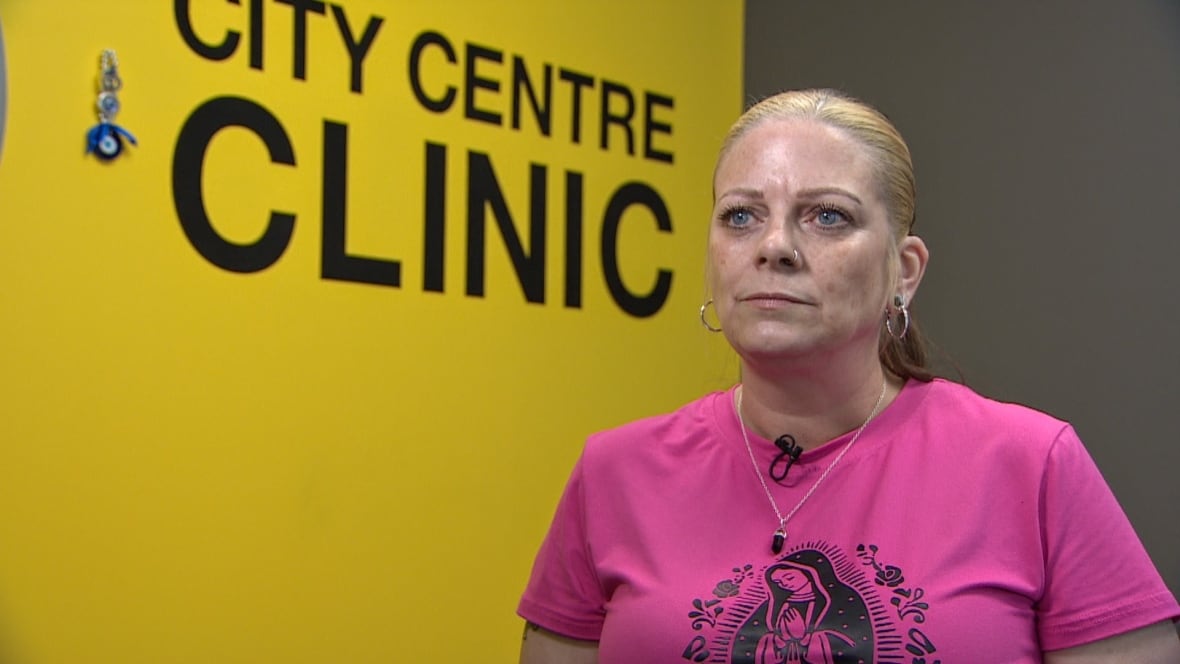 A woman in a pink shirt stands in front of a yellow wall