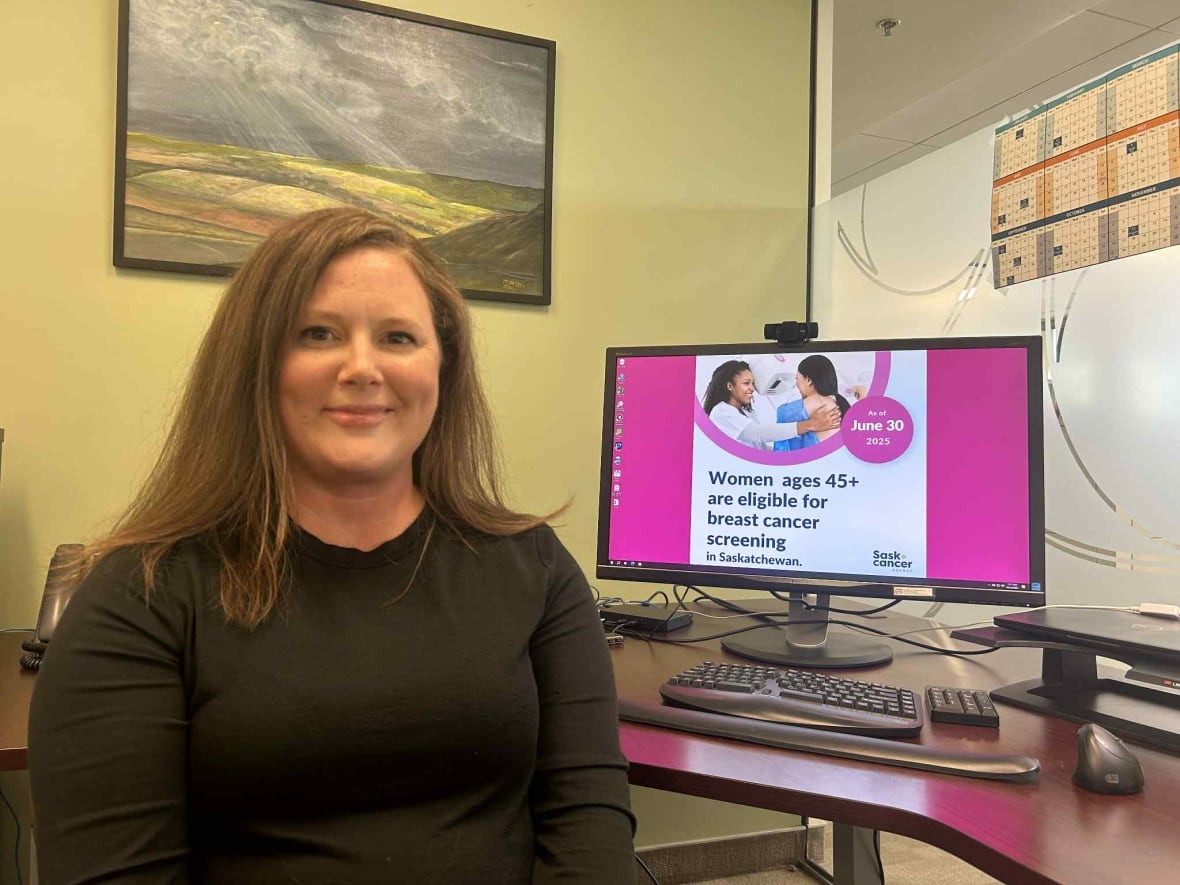 A woman in a dark shirt sits next to a computer showing a pink document.