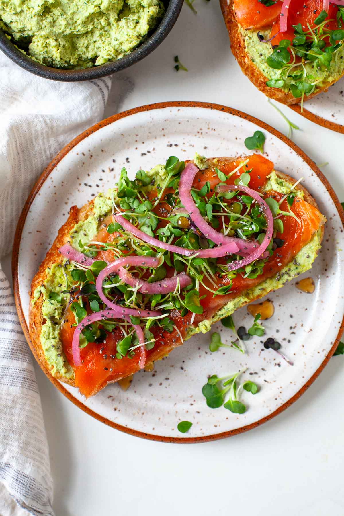smoked salmon toast with smashed edamame, pickled onions, honey, microgreens and chia on plate