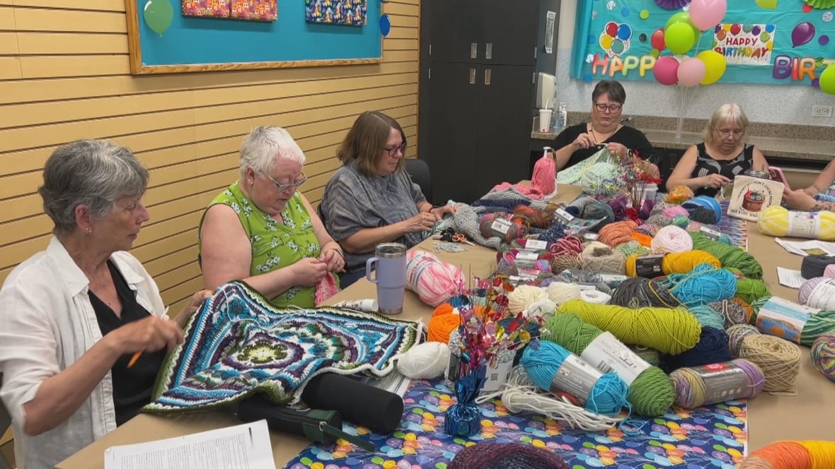 A group of women sit around a table full of yarn working on projects.